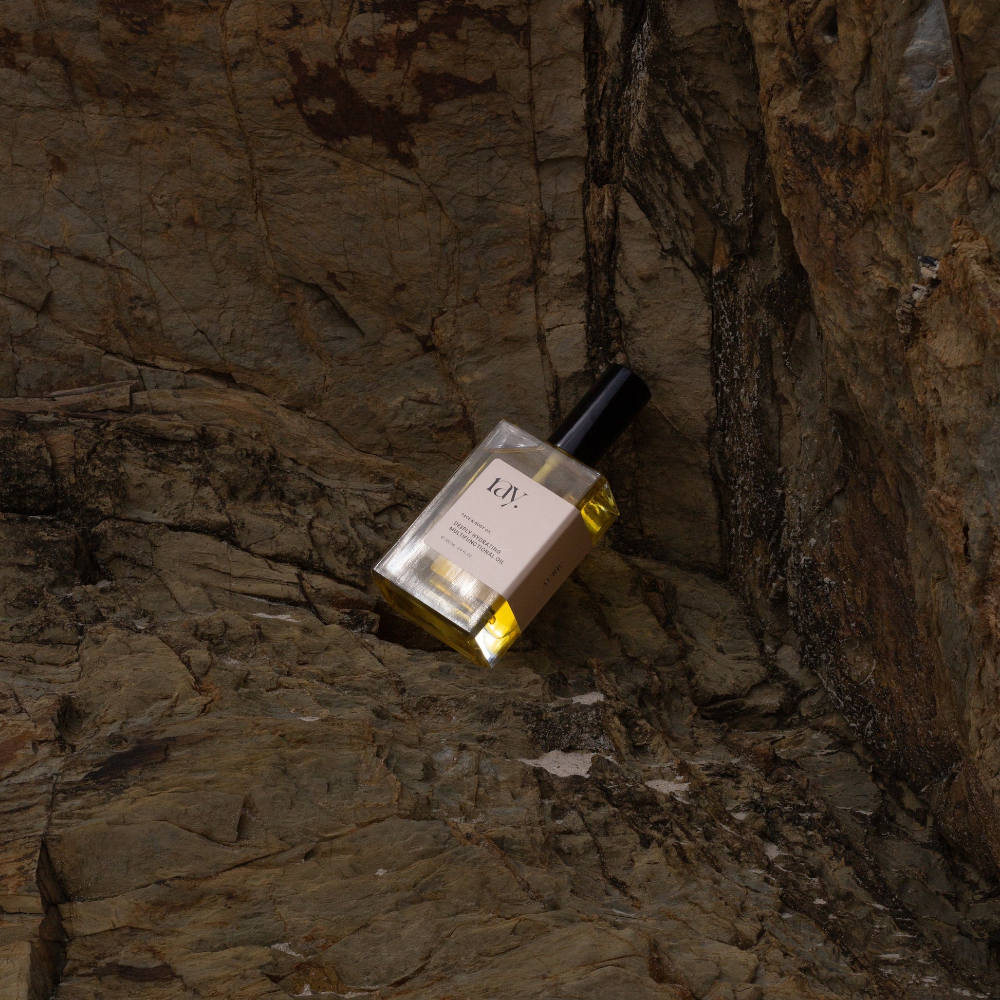 A natural hydrating body and face oil laying at the beach amongst organic rocks
