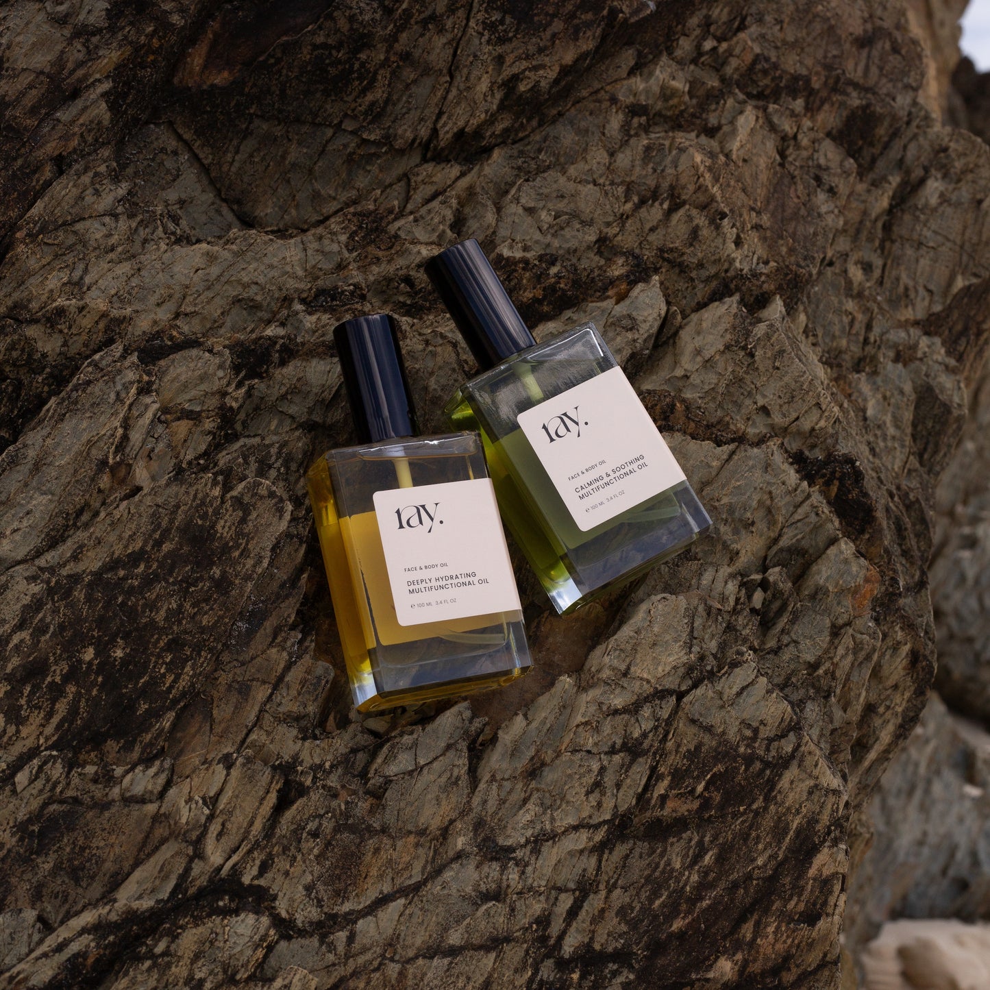 Two natural hydrating body and face oils coupled together on a rock face at the beach