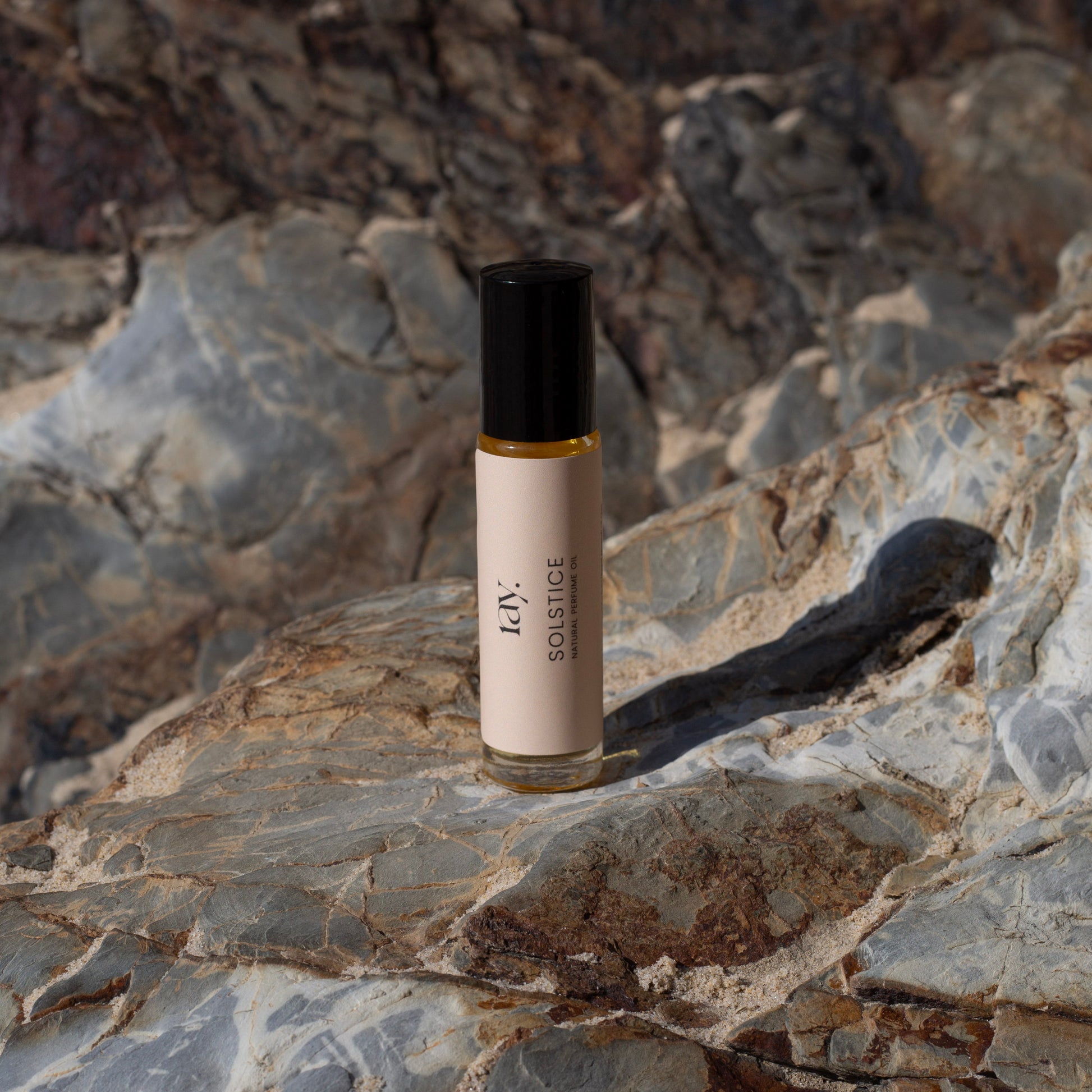 Travel size perfume roll-on oil standing on rock face at the beach